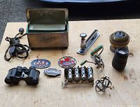 Lot overview showing all items on a wooden table outside on pavement, includes vintage Empire appliance, badges, stapler, wooden container, binoculars, napkin holders, hand mixer, bottle opener