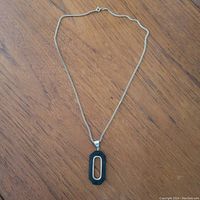 Full length view of sterling silver chain necklace with black geometric pendant on wood surface.