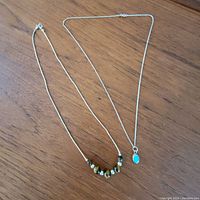 Two sterling silver necklaces on wooden surface; one with tiger's eye and silver beads, the other with turquoise pendant.