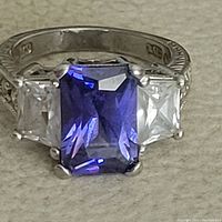 Close-up front view of sterling silver ring with purple center stone and clear side stones on band with engraving.