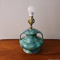 Front view of vintage ceramic table lamp with green mottled glaze, brass socket, and white bulb