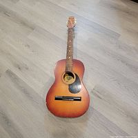 Full front view of the vintage guitar showing sunburst finish and wood body with pickguard and missing strings.