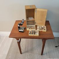 Overview photo showing vintage microscope, wooden cabinet case with open door, and three wooden trays with mineral specimens on a table.