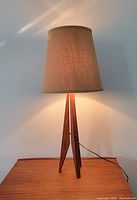 Full view of lamp showing tripod teak base and fabric shade illuminated