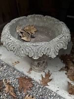 Top view of the concrete planter or bird bath showing detailed scalloped edge and weathered interior with some leaves inside.