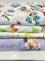 Stacked view of four folded vintage double flat sheets featuring different floral patterns including mauve flowers, strawberries, yellow bouquets, and cornflower blues.