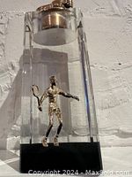 Front view of mid-century modern acrylic lighter with brass tennis player figure inside and brass lighter insert on top.