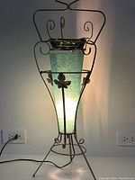 Front view of the illuminated floor ashtray showing the metal frame, green textured shade, and on top a green glass ashtray.