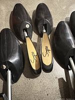 Six men’s shoe trees showing adjustable metal rods, branded wooden heel pieces (Simpson and Bally) on three pairs. Black wood/plastic toe sections with solid construction.