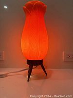 Lamp lit showing orange glow from molded shade on wooden tripod base