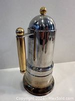 Front view of the moka coffee maker showing the brass handle and brass top knob on the domed lid.