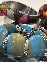 Close-up of chunky blue and yellow marbled bracelet with silver accents, showing detail on materials and color.