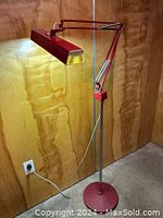 Full view of vintage Luxo articulating floor lamp lit up, showing the red metal body, articulated arm, and metal base.