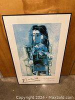 Front view of framed Picasso art print leaning against wooden door on concrete floor.