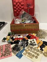 Woven sewing basket open showing assortment of buttons on cards and loose, wooden thread spools, and scissors attached to lid