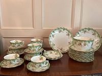 Overview of 8 cups on saucers displayed alongside plates and serving bowl