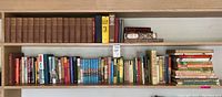 Wide view of bookshelf containing multiple rows of vintage and antique books, showing a variety of classic novels and literature collections.