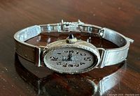 Oblique view showing oval dial with Arabic numerals and attached replacement metal bracelet