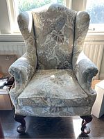 Front view of wing back chair showing floral upholstery and carved wooden legs.