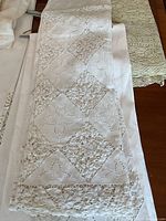 Folded white tablecloth showing alternating solid and cutwork diamond panels with floral motifs