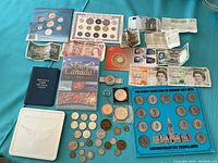 Overview of lot on teal fabric showing albums, booklets, banknotes, loose coins, medals, tokens and plastic coin tin