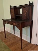 Angled front view of desk showing overall structure including drawers, cabinets, mirror, and tapered legs