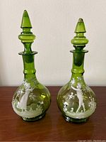 Two green glass decanters with stoppers shown side by side on wooden surface