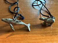Front view of whale and bear pendants on black cords laid flat on wood surface