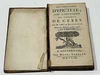 Opened book showing title page with the title 'Les Caracteres d'Epictete, avec l'explication du Tableau de Cebes', author M. l'Abbé de Bellegarde, and publication info Amsterdam, Chez Henri Schelte MDCCIX (1709). Also shows detached front board lying alongside.