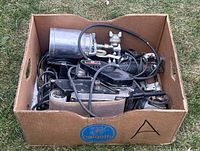Box filled with various power tools including Porter-Cable drill, belt sander, and other tools with cords tangled together.