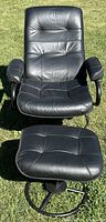 Front view of black reclining lounge chair and ottoman on grass, showing tufted cushions and padded armrests