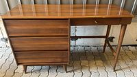 Front view of Mid-Century Modern wooden desk showing 4 drawers on the left and 1 drawer on the right with tapered legs.