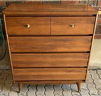 Front view of the wooden mid-century modern dresser showing four drawers with brass knobs and tapered legs.