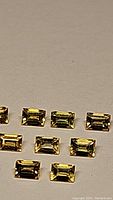 Top-down photo showing 10 baguette cut canary yellow natural sapphires arranged in two rows on a neutral surface.