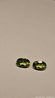 Pair of two oval-cut apple green Peridot gemstones placed on a plain surface showing the color and cut.
