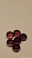 Photo showing six round cabochon pink-purple garnet gemstones arranged on beige surface
