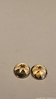Pair of round cut golden citrine gemstones with faceted dome shapes shown against plain background.