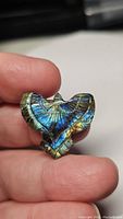 Close-up of the natural labradorite eagle carving showing strong blue and golden flash with visible feather detail on a polished surface held between finger and thumb.