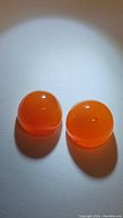 Photo of two round Mandarin Carnelian cabochon gemstones side by side on white background with light reflection showing smooth dome shape and vibrant orange color.