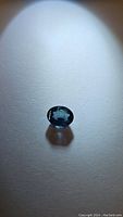 Oval cut natural blue sapphire gemstone lying flat, showing its deep blue color and clean facets under light.