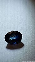 Oval cut natural blue sapphire gemstone shown with visible color zoning and polished facets.