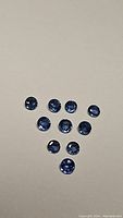 Ten round cut natural blue sapphires arranged on a light solid background showing color and clarity.