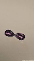 Two pear-shaped purple amethyst gemstones on a neutral background showing facets and shape.