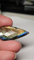 Close-up of the fancy cut labradorite held between fingers, highlighting the blue and golden flash and checkerboard facets.