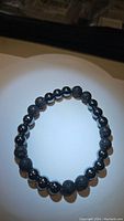 Black lavastone and hematite bead stretchy bracelet laid flat in a circular shape, showing alternating stone textures.