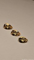 Three pear cut golden citrine gemstones displayed on a plain surface, highlighting their clarity and cut.