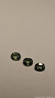 Photo showing three natural oval cut green apatite gemstones on a plain background, highlighting color and clarity.