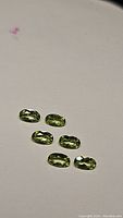Six natural apple green oval cut peridot gemstones spread loosely on a flat surface, showing shape and color.