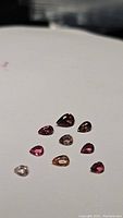 Nine pear-shaped pink tourmaline gemstones on a plain surface showing different shades and clarity