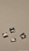 Four natural white topaz square and emerald cut gemstones placed on neutral background.
